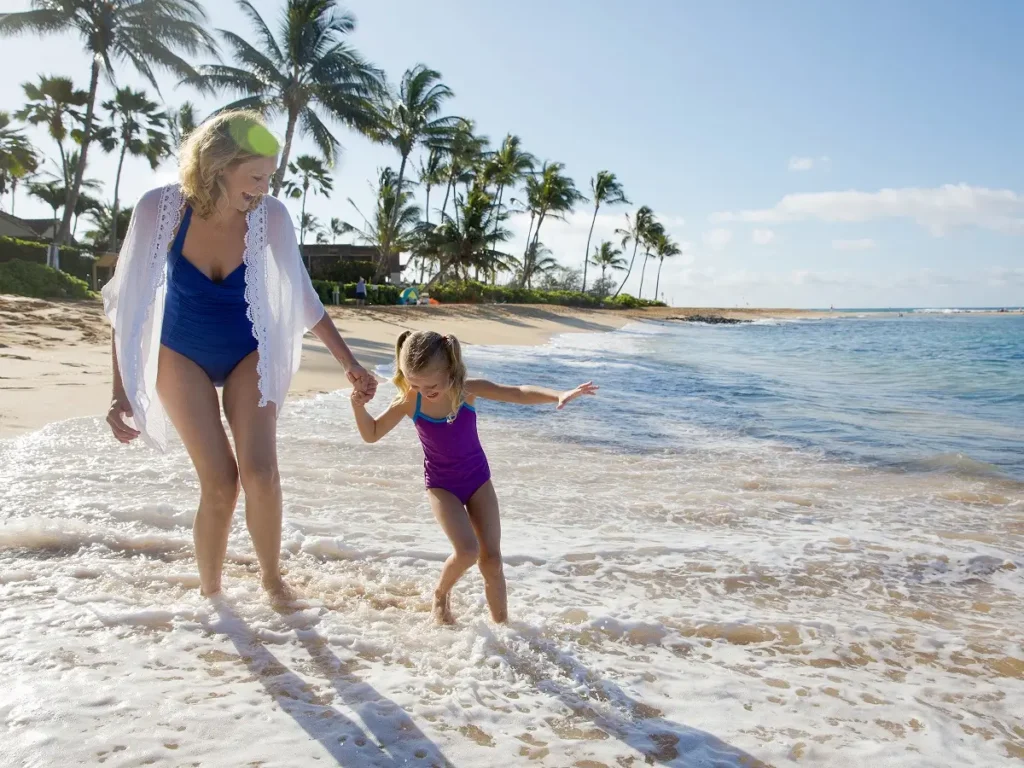 A mother and daughter laughing on the beach standing in the water.
