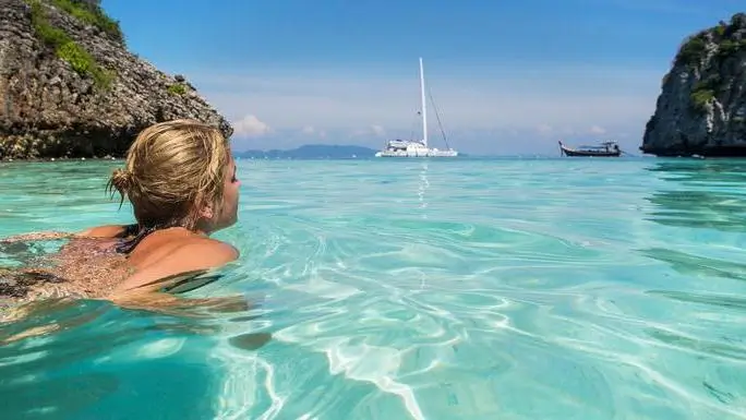 Woman swimming in clear waters with a sailboat in the background during a 7-day sailing trip in Thailand.