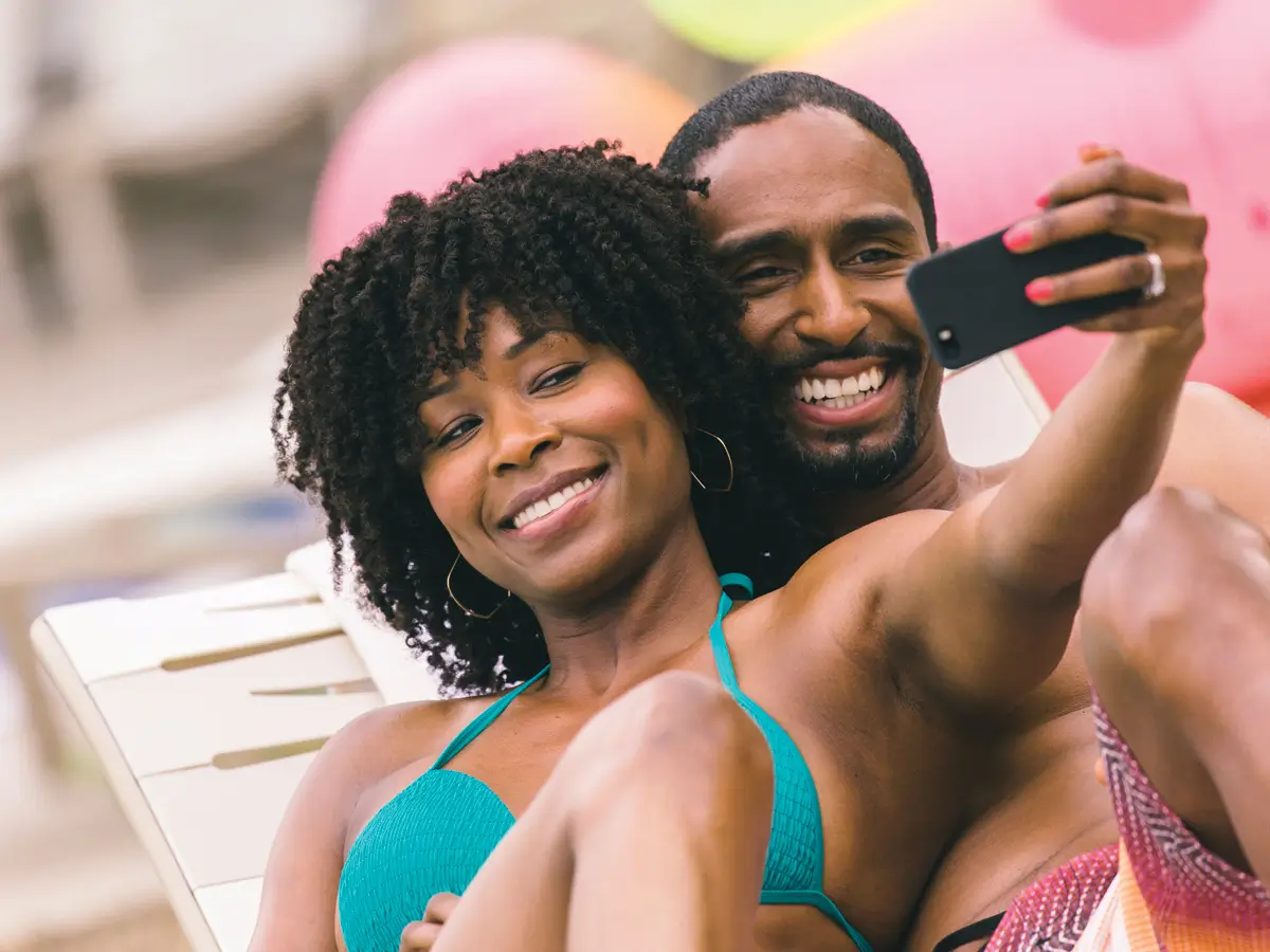 Couple at a pool smiling and taking a selfie with mobile phone.